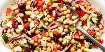 chickpeas with olives, feta, cucumbers, sliced red onion, and red bell peppers on a white platter