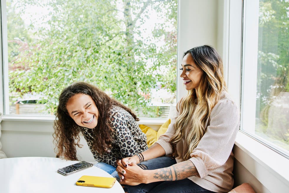 medium shot of mother and daughter laughing together while hanging out in living room