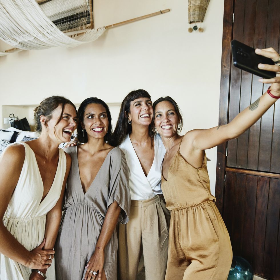 medium wide shot of smiling and laughing bridesmaids taking selfie in luxury hotel suite before wedding