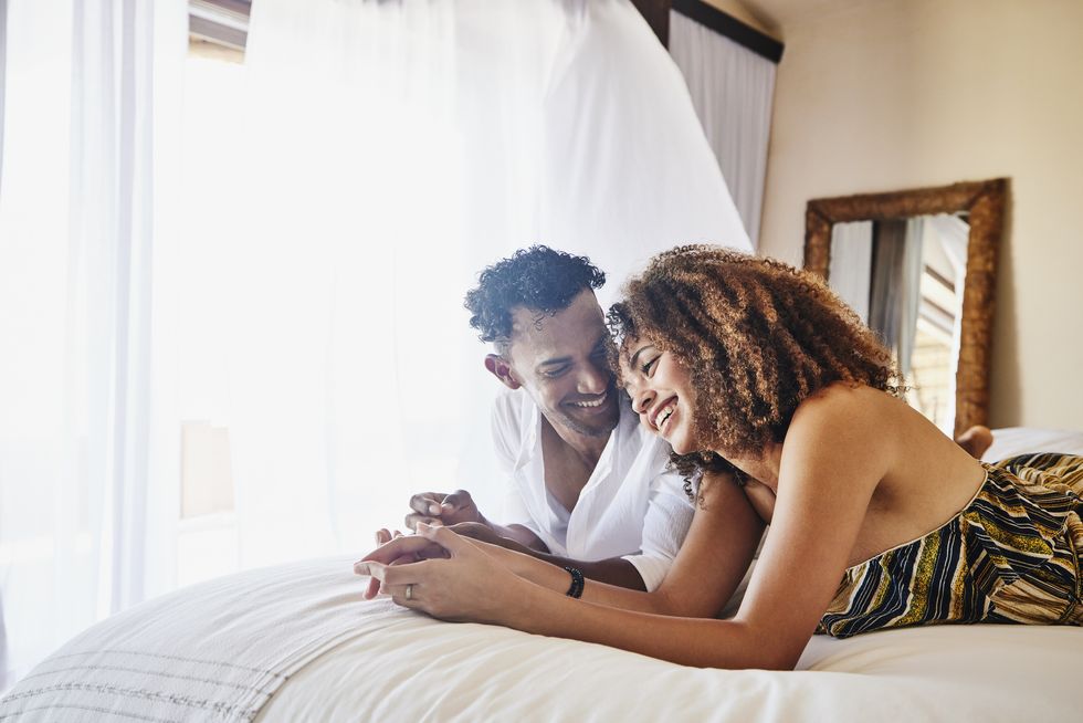 medium wide shot of smiling couple relaxing on bed in luxury suite at tropical resort