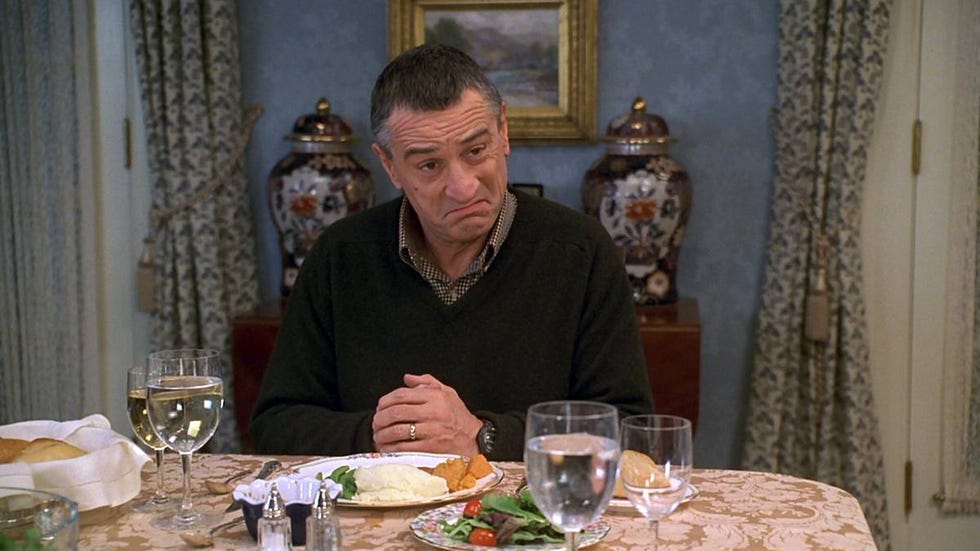 robert de niro in meet the parents, dining scene with a male figure seated at a table with various food items and drinks