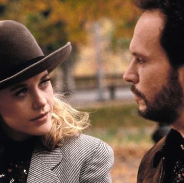 meg ryan in bowler hat and black and white striped jacket with padded shoulders looking at billy crystal in beard and brown leather jacket they are sitting outside in fall and looking serious