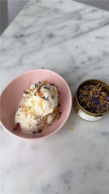 meghan markle as ever flower sprinkles scoop of ice cream topped with edible flowers in a pink bowl next to a tin of dried flowers