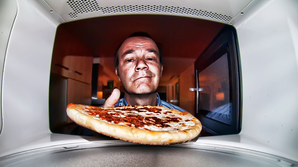 un hombre metiendo una pizza en el microondas