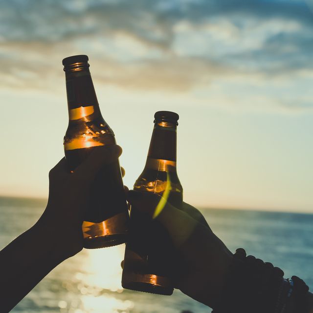 dos personas brindan con botellines de cerveza en una playa al atardecer