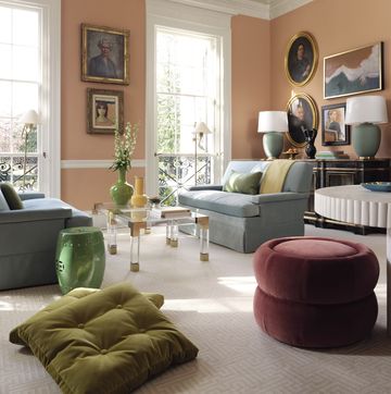 living room, orange walls, art on walls, maroon ottoman, green cushions