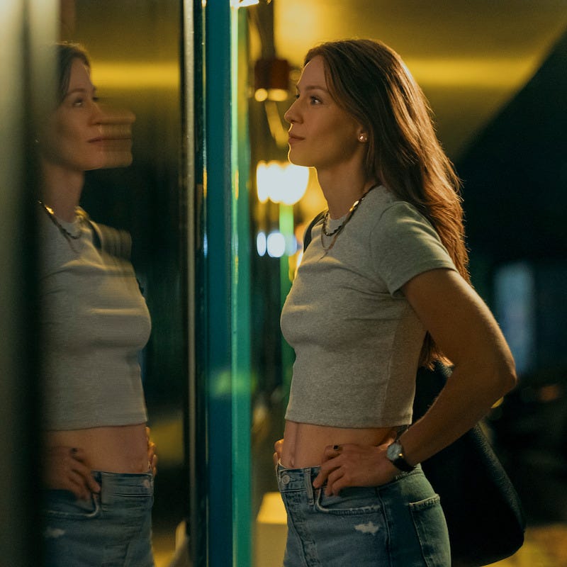 Una mujer parada cerca de una superficie reflectante mostrando su atuendo casual.