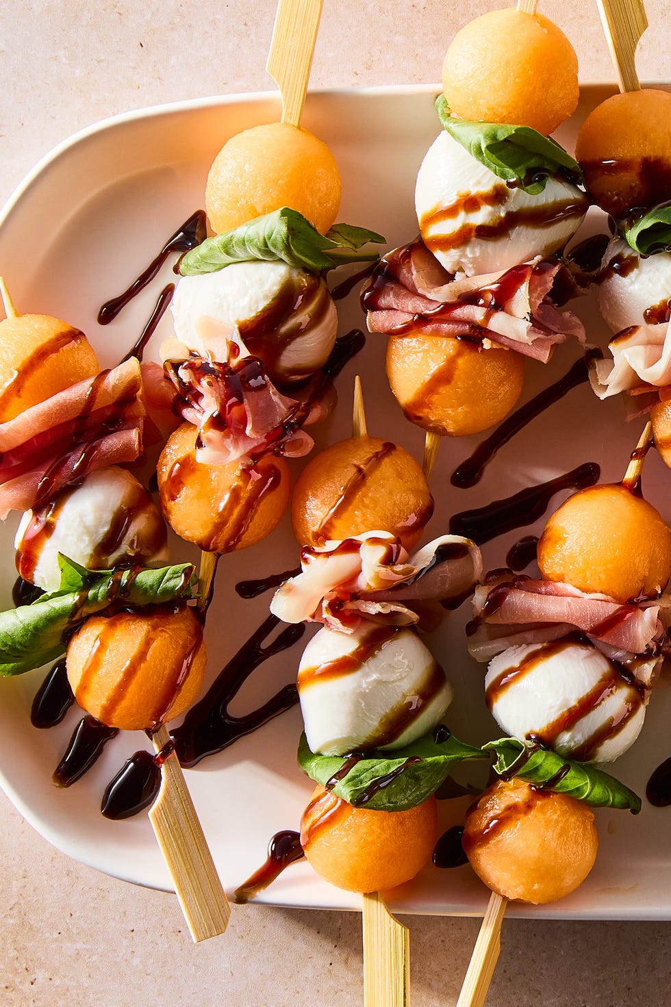 Melon and prosciutto skewers Skewers of cantaloupe balls, mozzarella balls and fresh basil leaves with balsamic sauce
