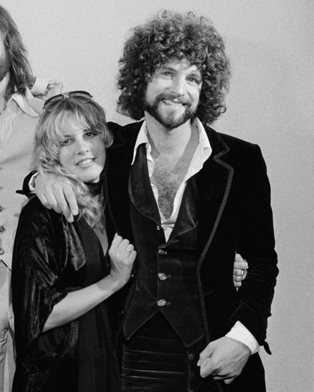 steve nicks and lindsey buckingham smile at the camera embracing each other in this black and white photo