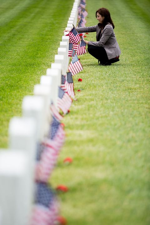 a woman touching a gravestone in a row of graves with small flags in front of them