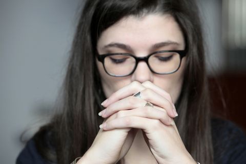 a woman with glasses praying with her hands folded in front of her mouth