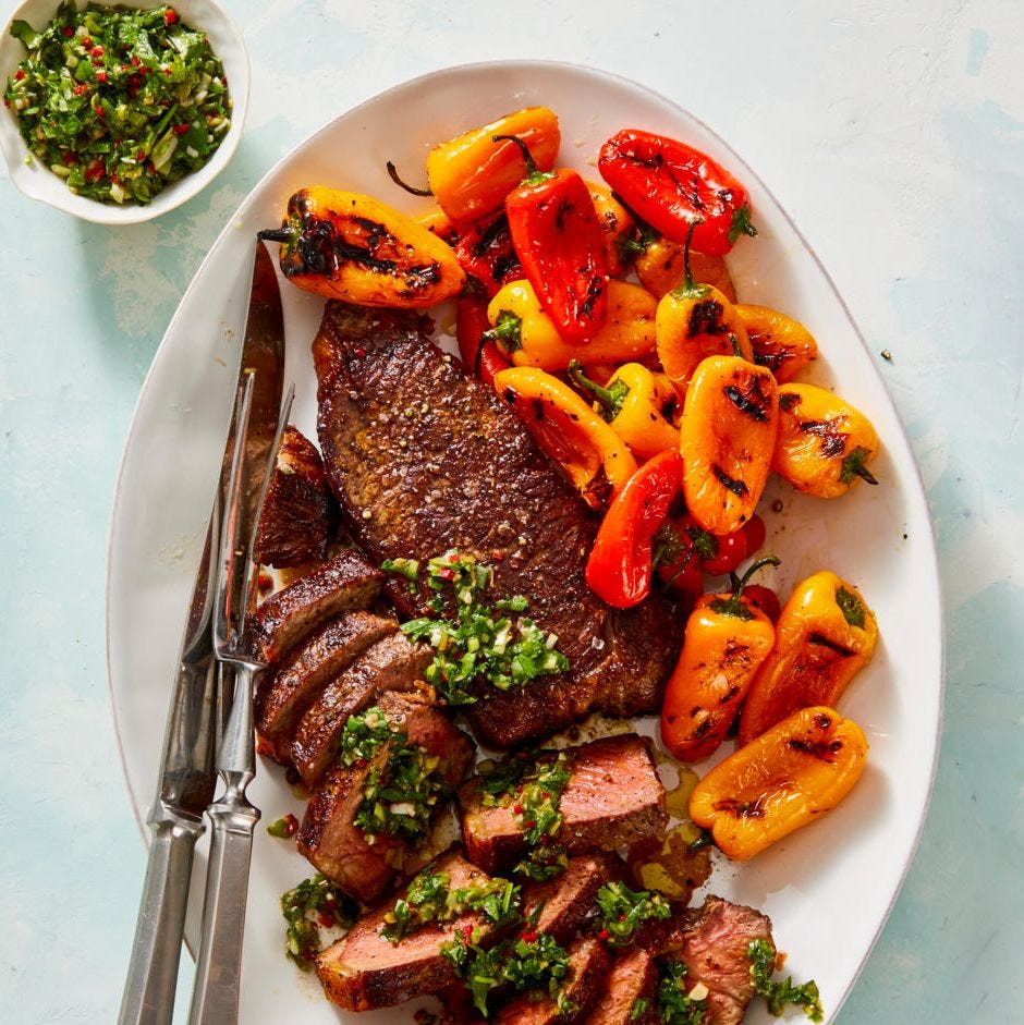 grilled steak and peppers with herb chimichurri sauce on a white plate