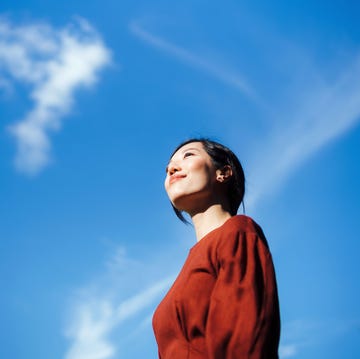 Low angle portrait of beautiful smiling young Asian woman standing against beautiful clear blue sky, looking up to sky enjoying nature and sunlight. Freedom in nature. Connection with nature low angle portrait of beautiful smiling young asian woman standing against beautiful clear blue sky, looking up to sky enjoying nature and sunlight freedom in nature connection with nature