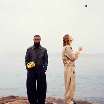 a man and woman standing on a cliff with a body of water behind them