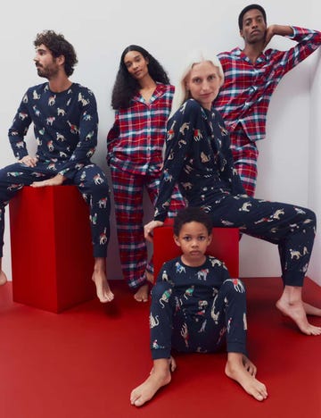 group of five individuals in festive pajamas posing on a red backdrop