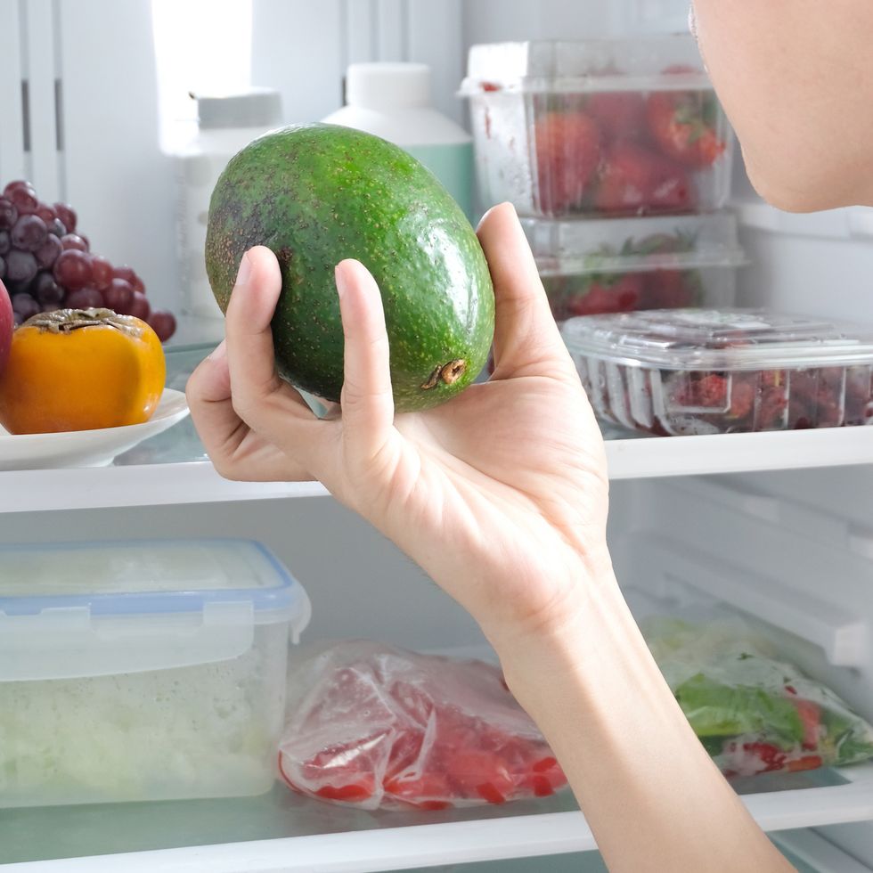 men selection ingredients for good health, holding an avocado make a health food. health care by eat clean food consist of fruits, vegetable, apple , strawberry and tomato and grape inside the fridge.