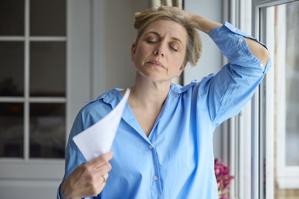 menopausal mature woman having hot flush at home cooling herself with letters or documents