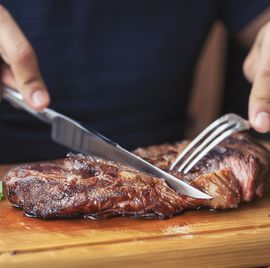 men's hands holding knife and fork, cutting grilled steak