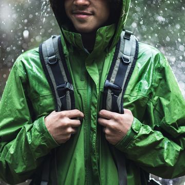 man standing in rain with backpack and green rain jacket