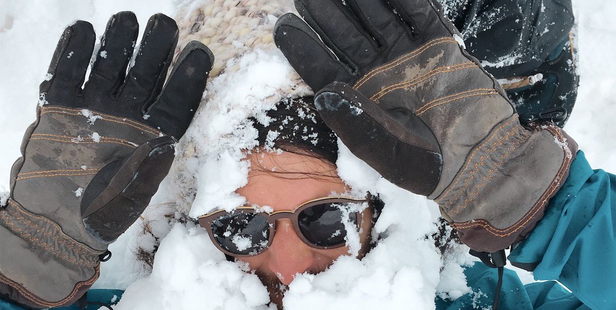 man buried in snow holding gloved hands up