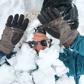 man buried in snow holding gloved hands up
