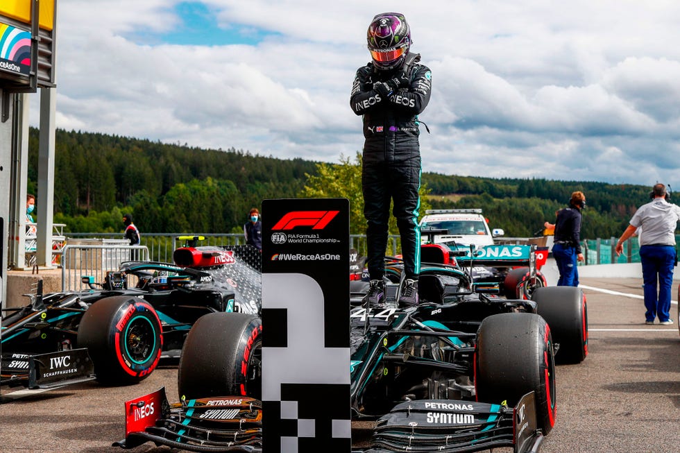 lewis hamilton stands on top of his racecar and crosses his arms in an x across his chest