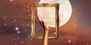 a hand holds up a full moon inside a golden picture frame over a background of a dark, starry sky