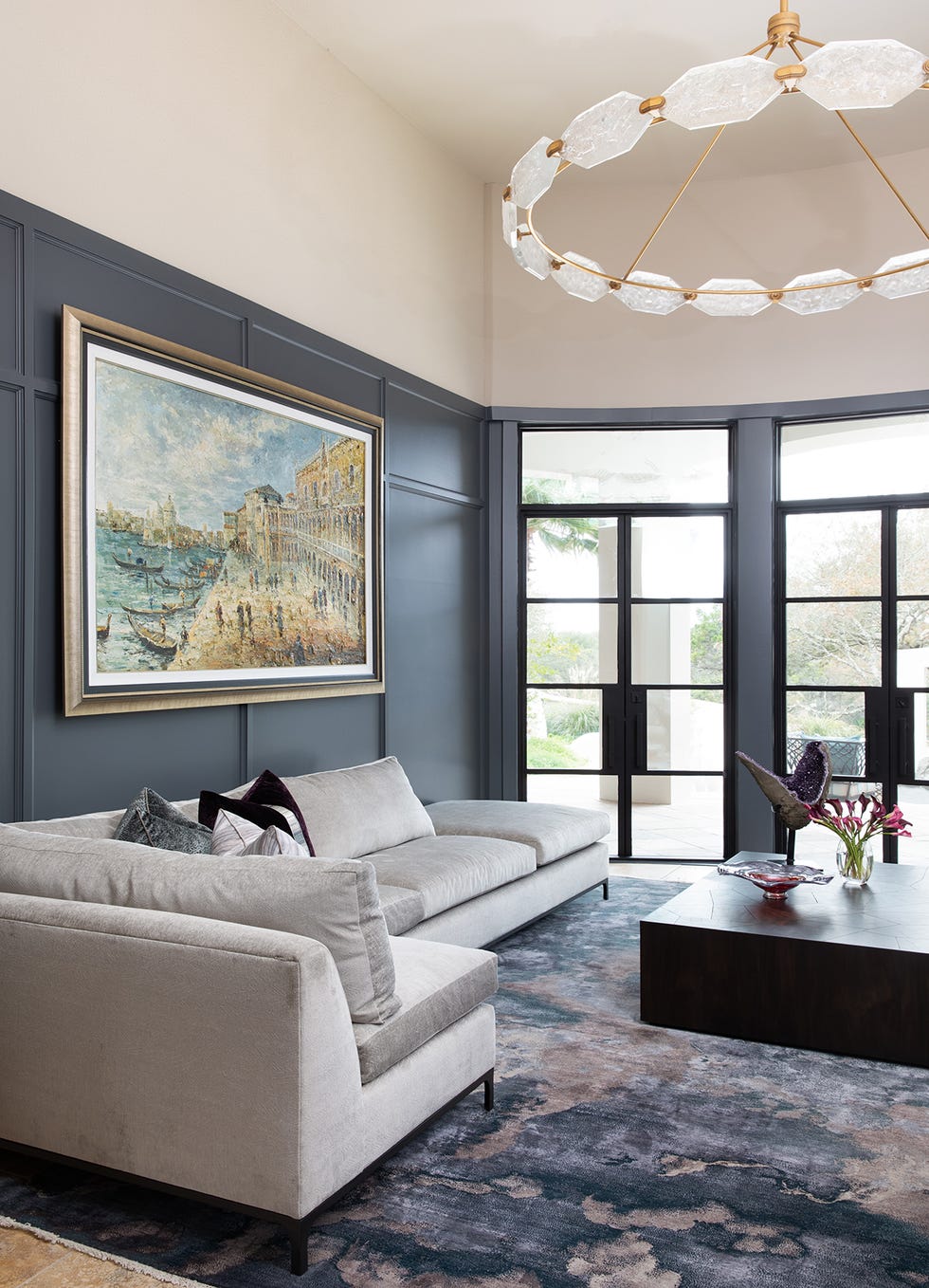 a living room with a chandelier, a gray couch and blue abstract rug