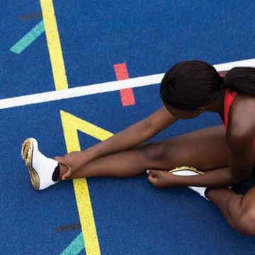 vrouw stretcht zittend op atletiekbaan