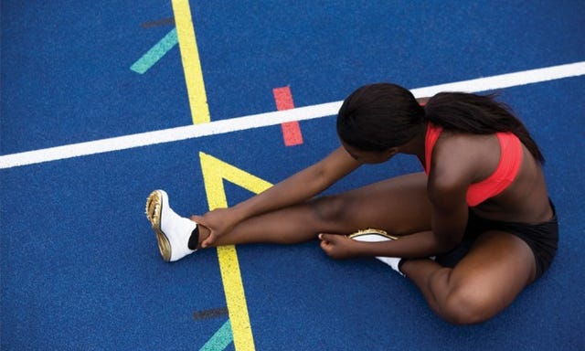 vrouw stretcht zittend op atletiekbaan