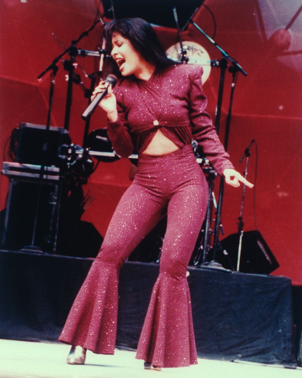 a woman in a monochrome red sparkling outfit sings into a wireless microphone she holds in one stand as she stands on a stage
