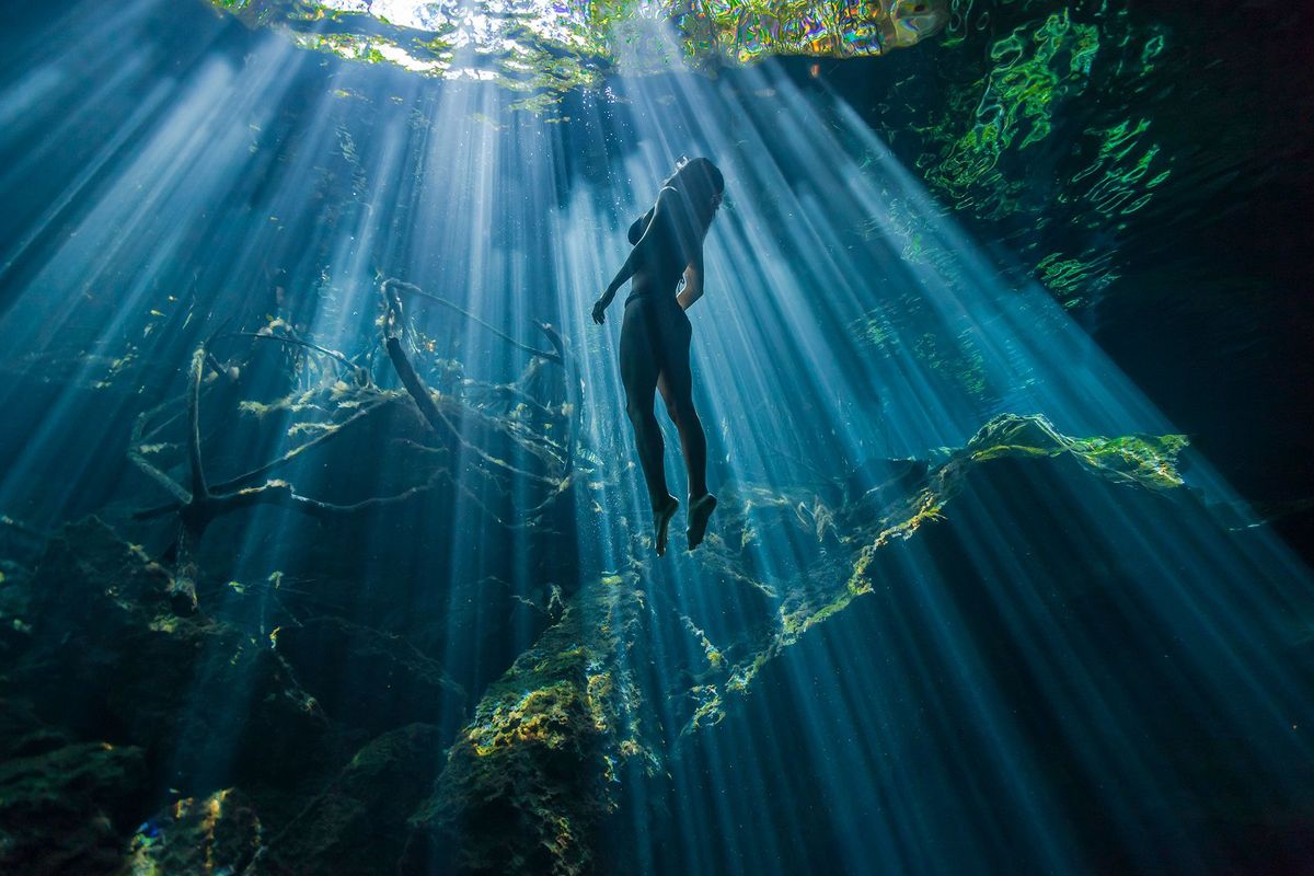 Een zwemmer zweeft door zonovergoten water in een van Yucatans vele kalkstenen zinkgaten