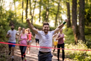 successful young man running through finish line and celebrating victory with arms raised