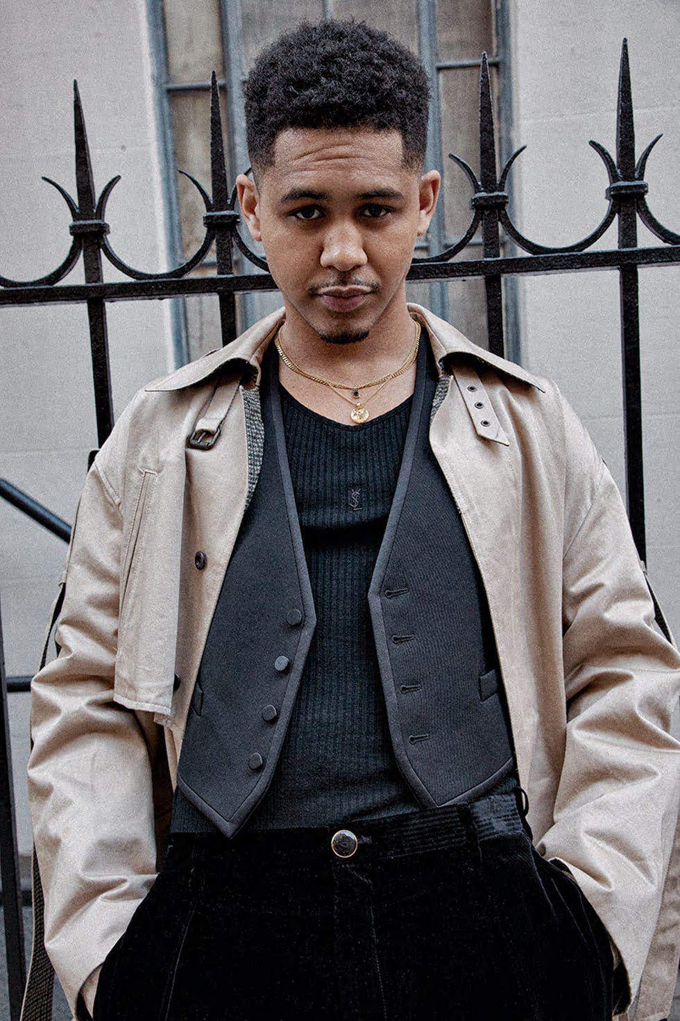 Person in a layered outfit with a decorative fence in the background