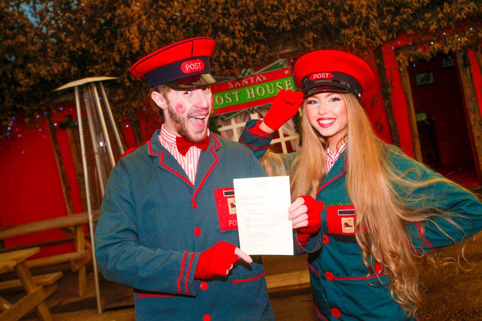 Two individuals in festive outfits hold a letter addressed to Santa