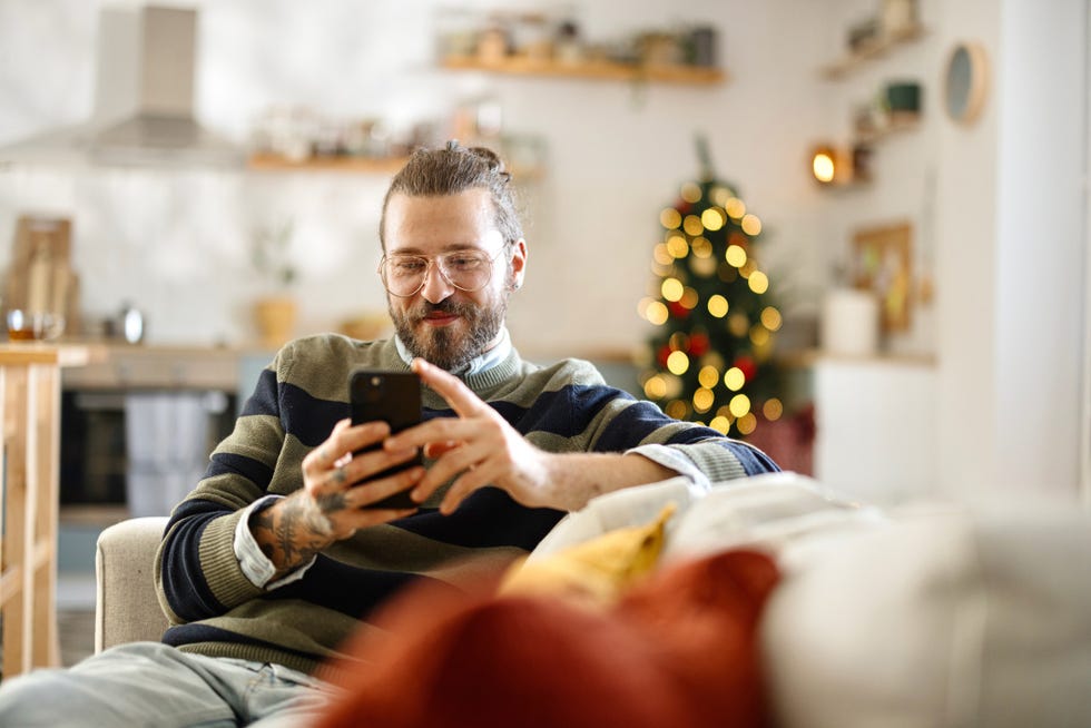 person sitting on a couch using a smartphone with a decorated christmas tree in the background