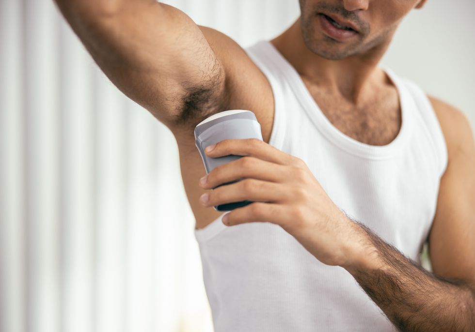young male applying deodorant to armpit at his apartment stock photo