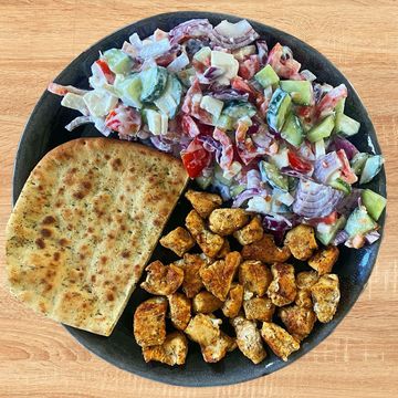 bord met naanbrood, salade en gekruide kipfiletblokjes