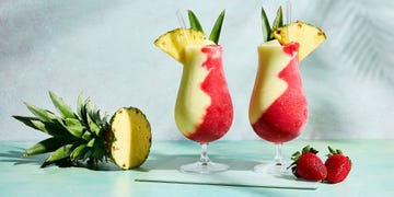 pina colada and strawberry daiquiri divided in glass topped with pineapple wedge and leaves