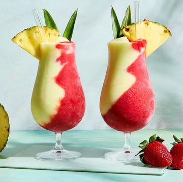 pina colada and strawberry daiquiri divided in glass topped with pineapple wedge and leaves