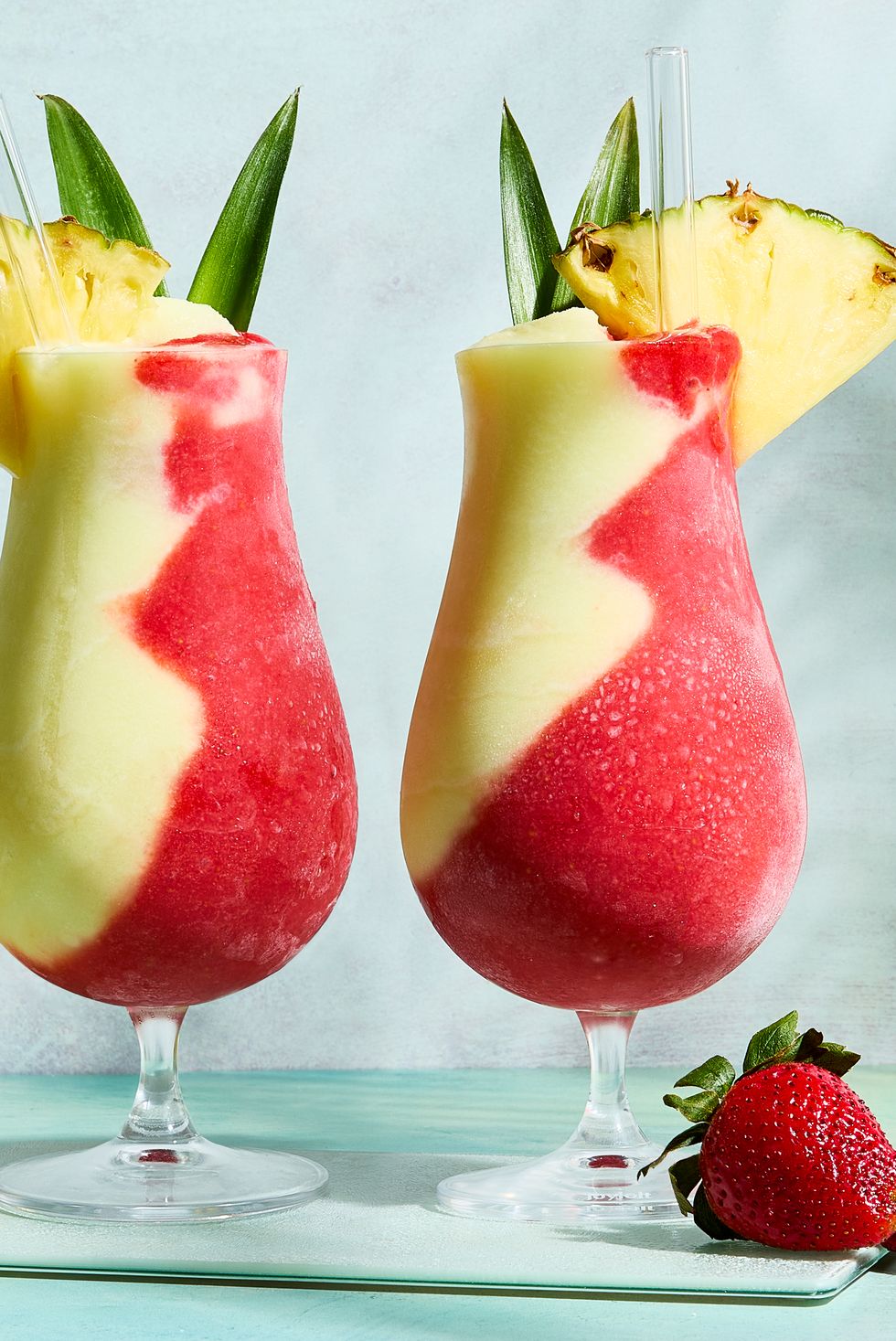 pina colada and strawberry daiquiri divided in glass topped with pineapple wedge and leaves