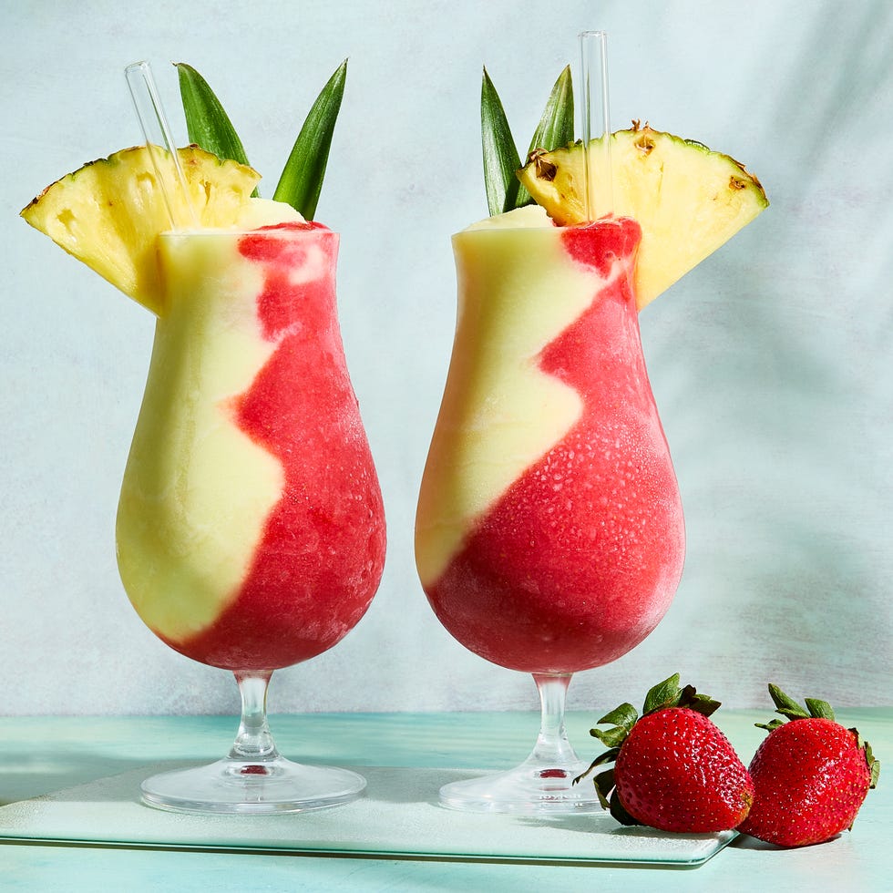 pina colada and strawberry daiquiri divided in glass topped with pineapple wedge and leaves