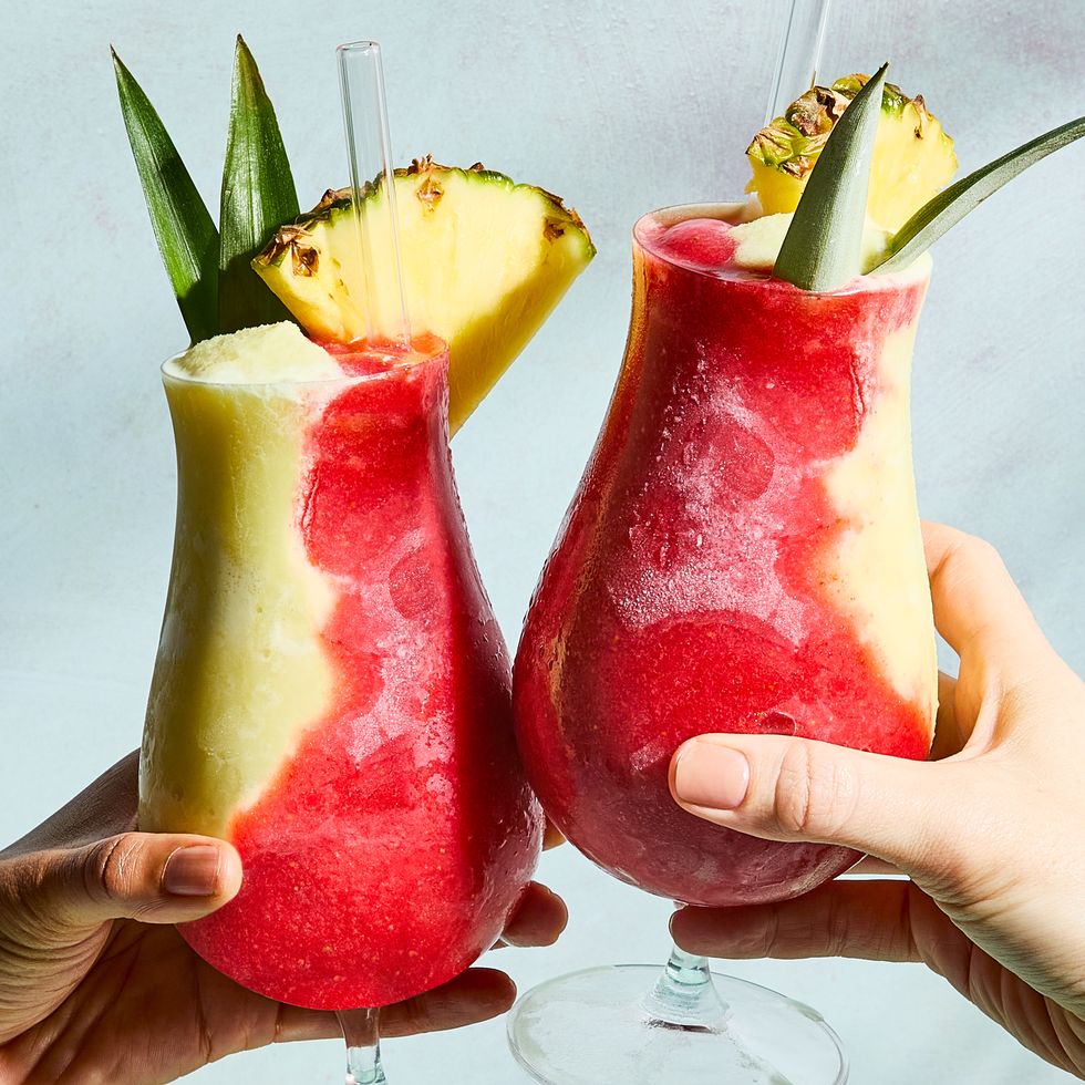 layered strawberry and pineapple frozen cocktail topped with a pineapple wedge and leaves