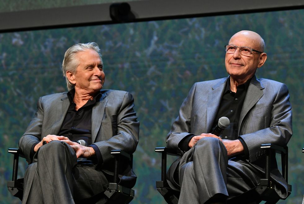 michael douglas and alan arkin, wearing gray suits and black shirts, sitting on chairs on a stage