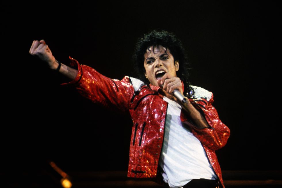 michael jackson wearing a red coat and white shirt, singing on a stage into a microphone