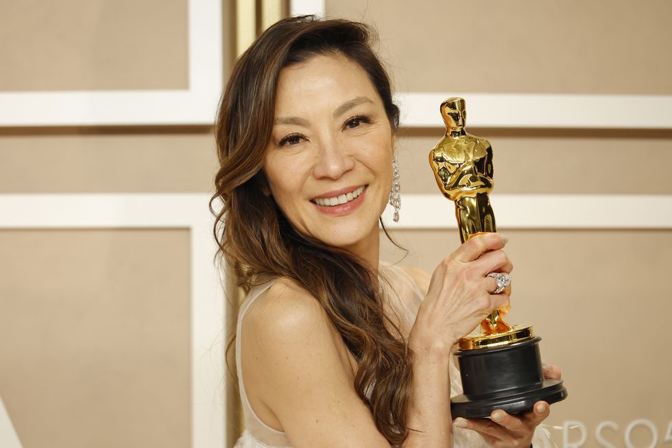michelle yeoh smiles and holds an academy award in a press room