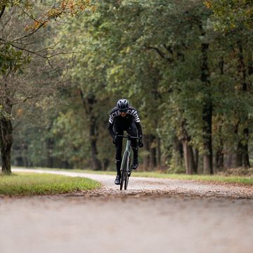 een wielrenner op een racefiets op een pad omringd door bomen