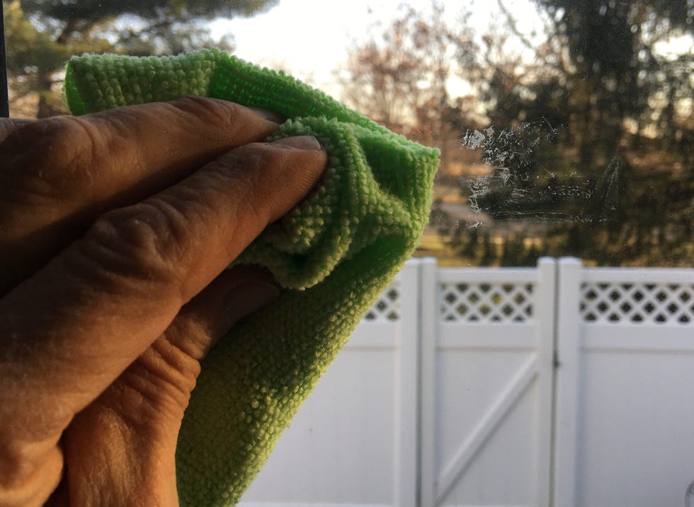 soaking a microfiber with goof off and cleaning a window