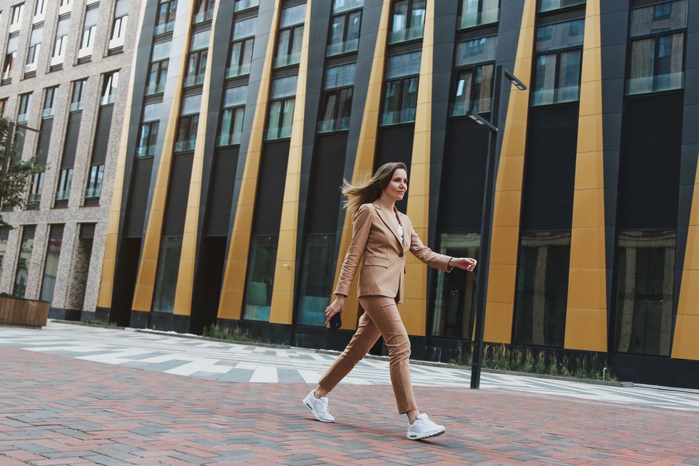 mid adult businesswoman wearing beige pantsuit walking fast next modern office buildings