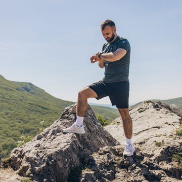 Mid adult man checking his smart watch after reaching the top of the hill running mid adult man checking his smart watch after reaching the top of the hill running